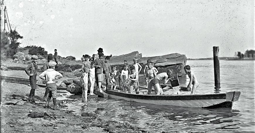 Group of boys bailing out a rowboat on the beach (Группа мальчиков вычерпывают воду из лодки на берегу), 1897-1905