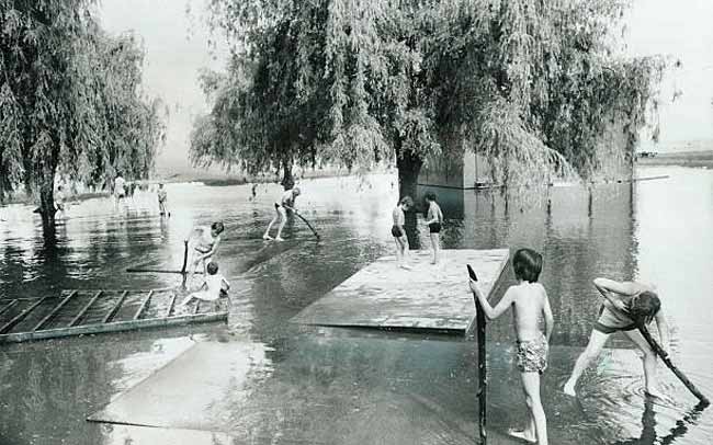 Boys use sections of the Coronation Park bandshell as rafts yesterday in a flooded section of the park (Мальчики используют секции эстрады Коронационного парка в качестве плотов на затопленном участке парка в наводнение), July 1973